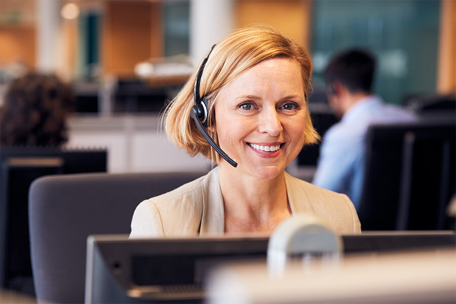 Female smiling whilst wearing a headset and working on a laptop