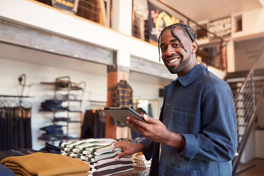 Male retail worker smiling whilst holding a tablet device