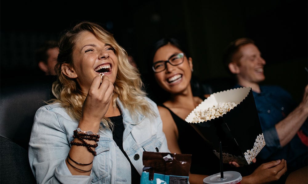 Two friends sat in the cinema laughing with popcorn